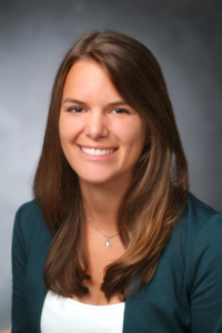 Junge Frau im grünen Blazer lächelt motiviert in die Kamera.