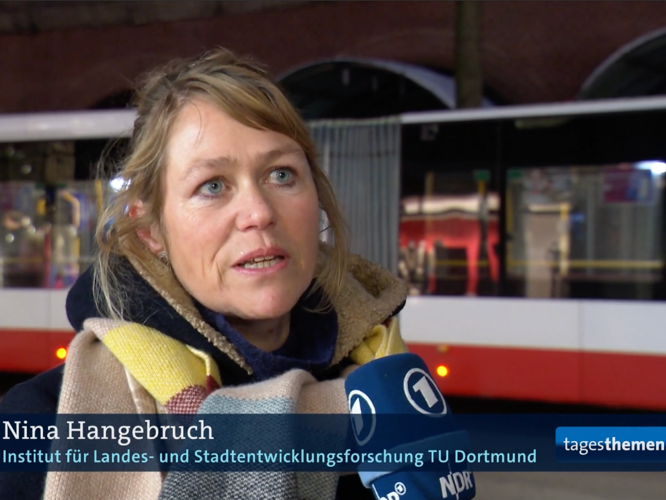 © Tagesthemen Nina Hangebruch spricht in ein Mikrofon, hinter ihr steht ein Bus.