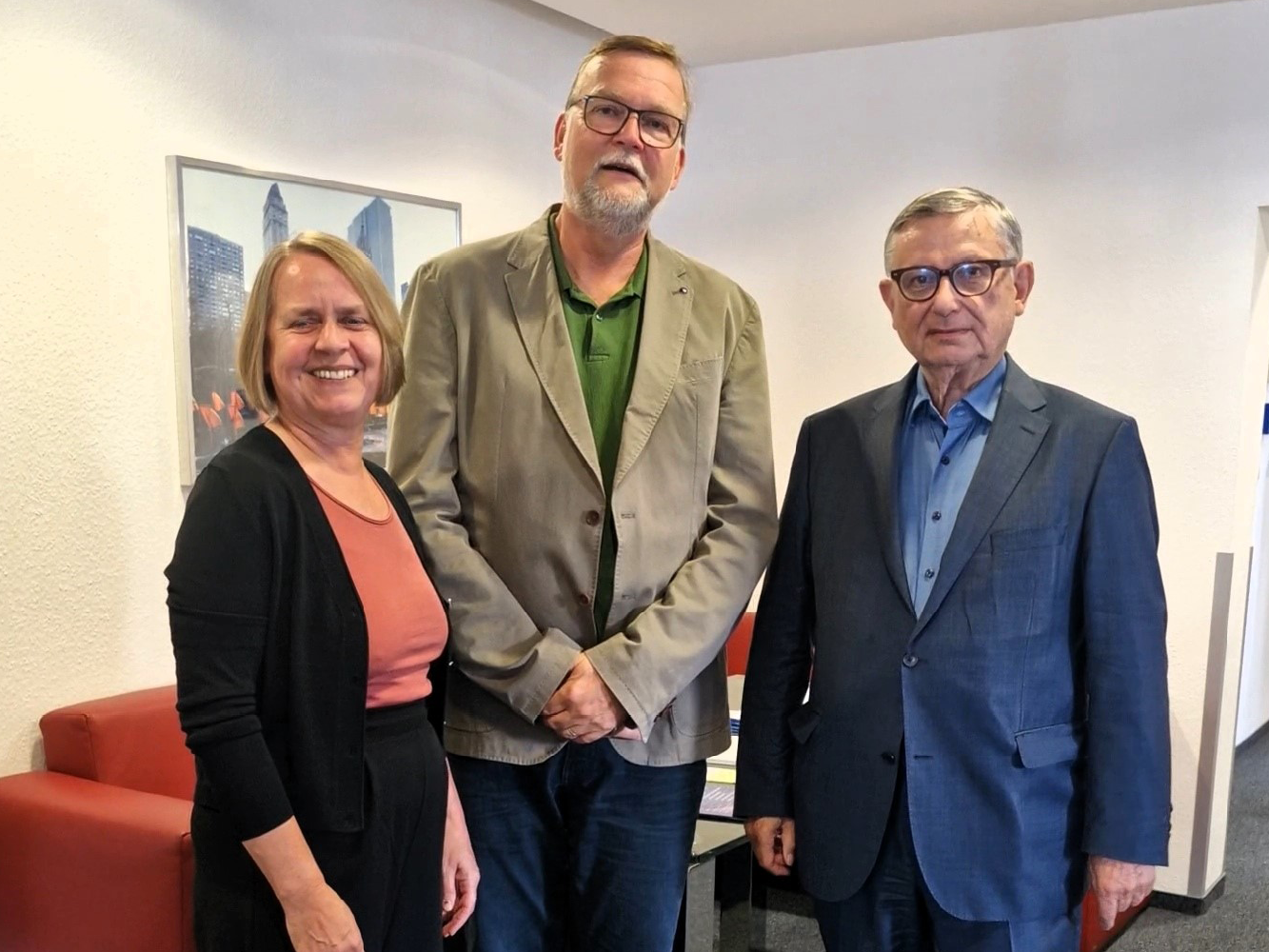 © ILS Christina Borbach, Ralf Zimmer-Hegmann und Christoph Zöpel stehen nebeneinander und lächeln in die Kamera. Hinter ihnen ist ein rotes Sofa und ein Bild an der Wand mit urbanen Gebäuden zu sehen.