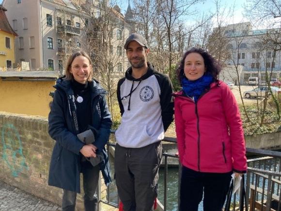 Drei Personen stehen vor einem Geländer und lächeln in die Kamera.