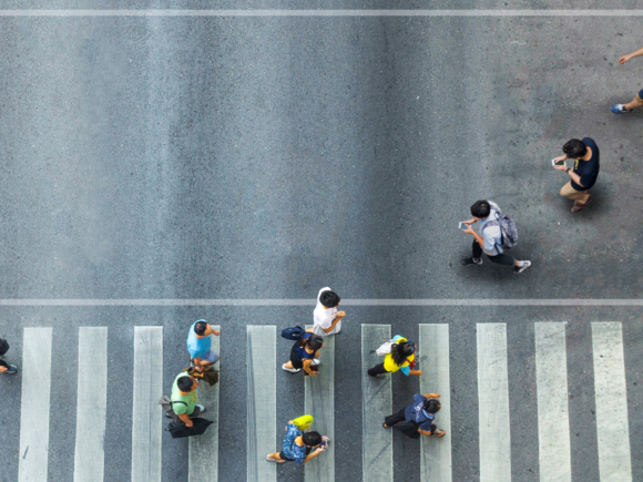 Menschen gehen über einen Zebrastreifen. Das Foto ist in der Vogelperspektive aufgenommen.