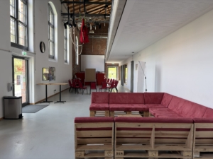 Ein Veranstaltungsraum mit weißen, hohen Wänden, einer Sitzecke mit dunkelroten Polstern.