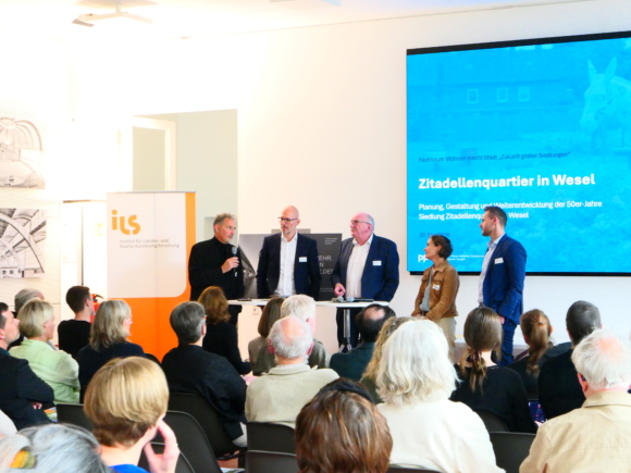5 Personen stehen vor einem Publikum und diskutieren.