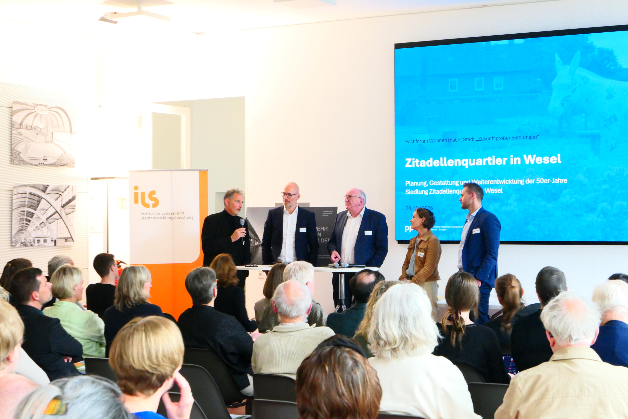 P1030716 5 Personen stehen vor einem Publikum und diskutieren.