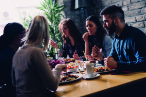 © AdobeStock_145799721 Mehrere Personen sitzen am Tisch und essen gemeinsam