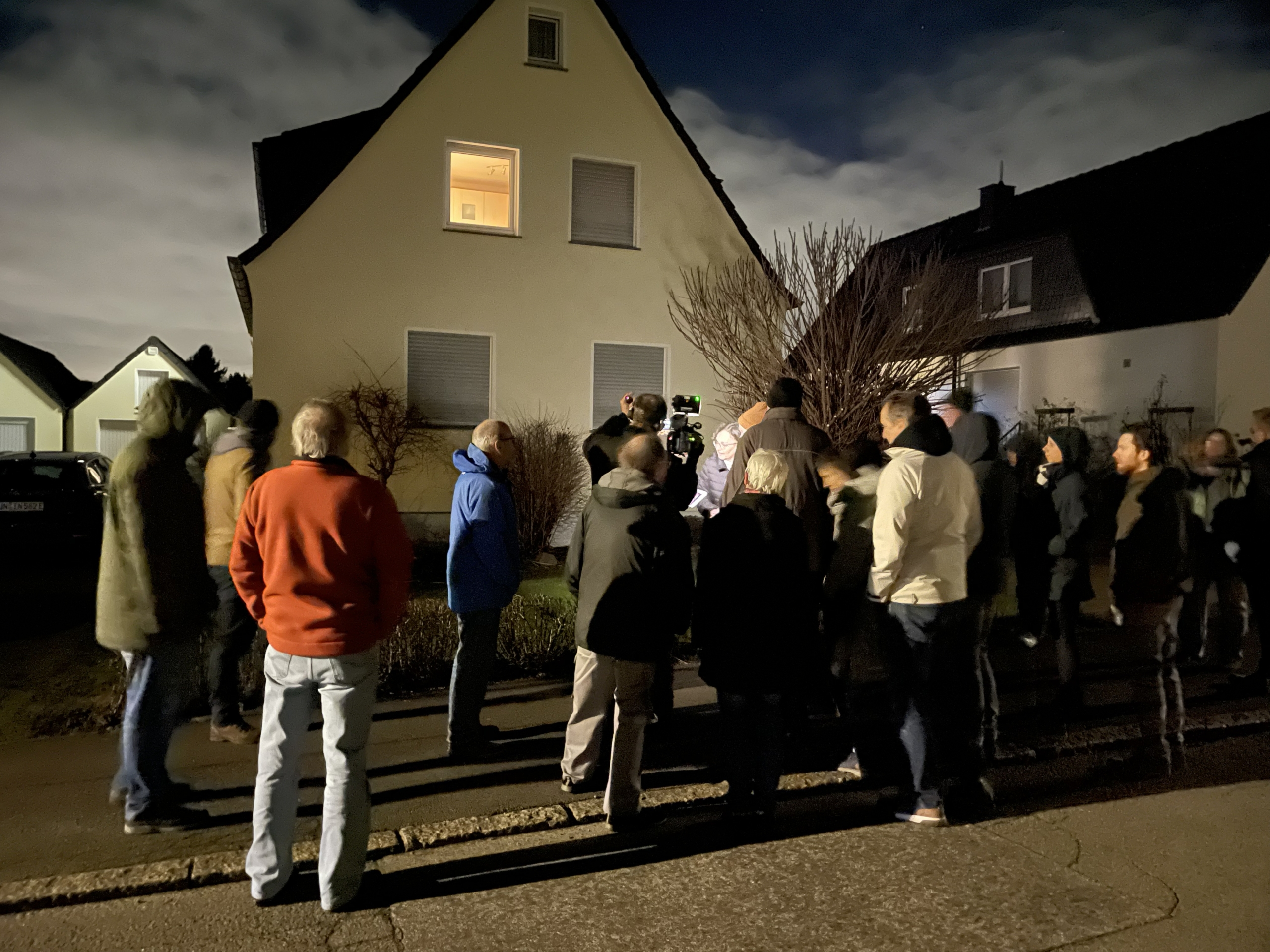 Eine Gruppe Menschen steht während der Dämmerung vor einem Einfamilienhaus