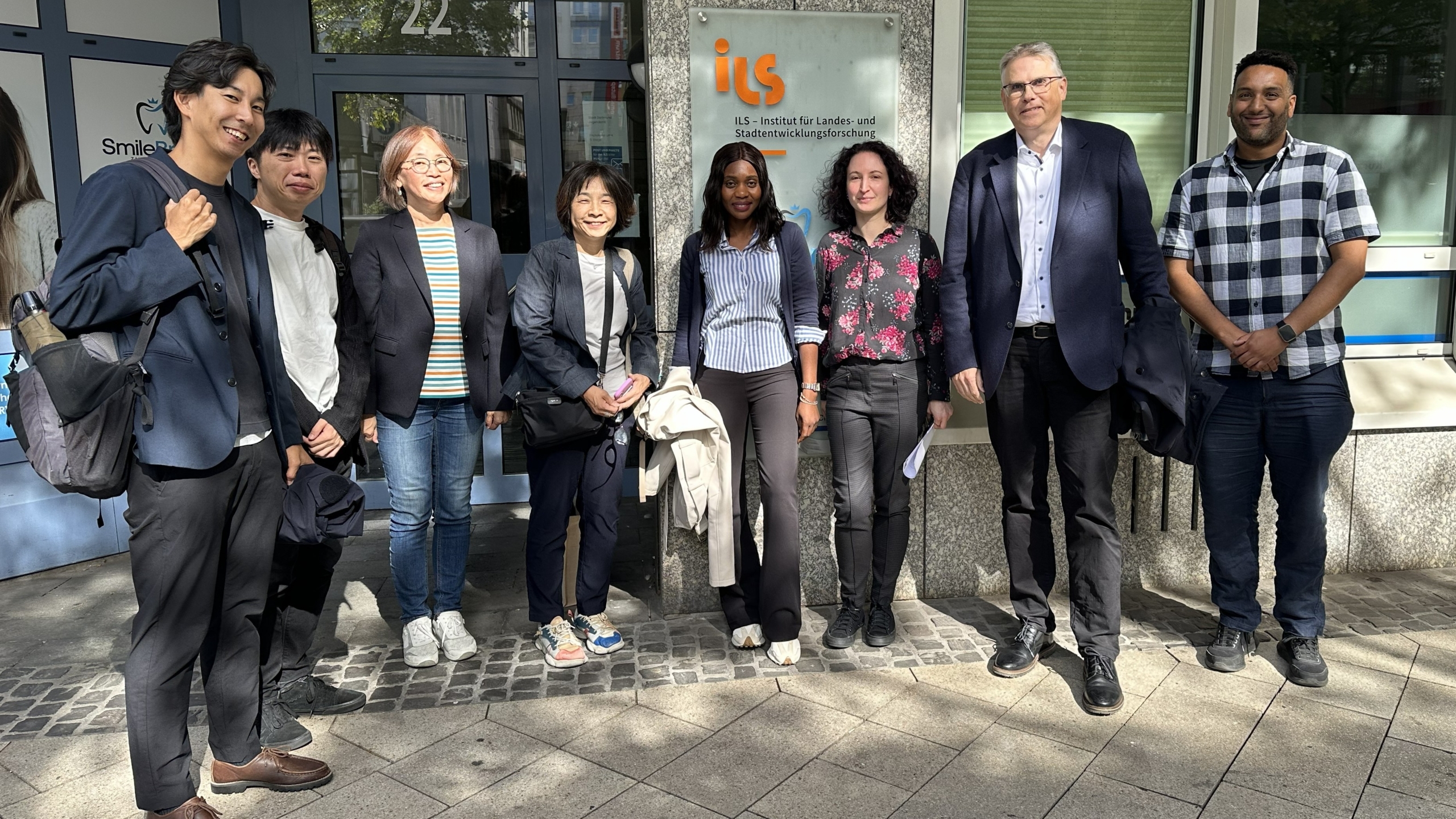 © Kleinmanns/ILS 8 Personen stehen vor einer Eingangstür und lächeln in die Kamera
